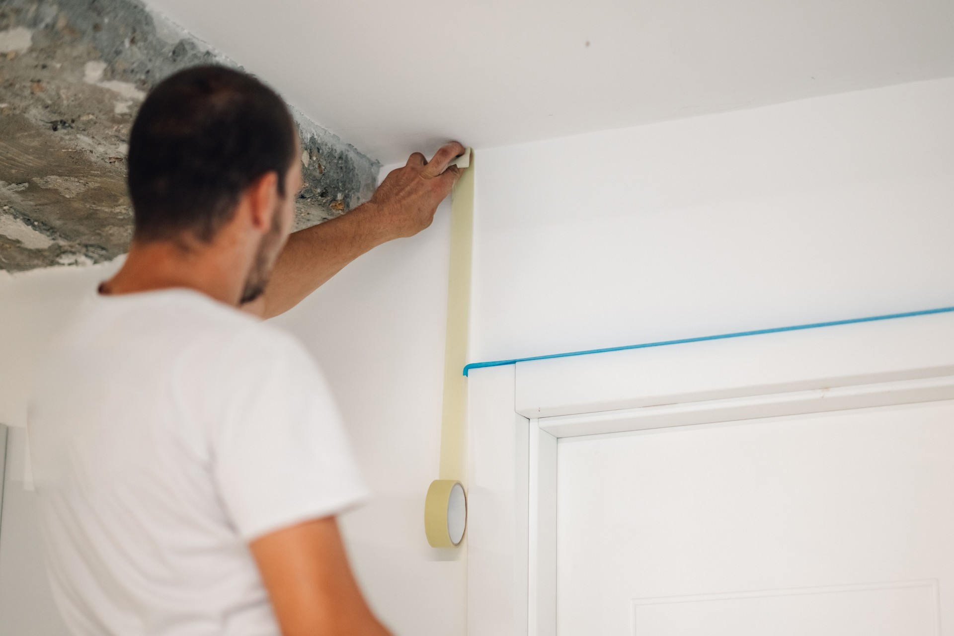 Painter applying masking tape on wall before painting